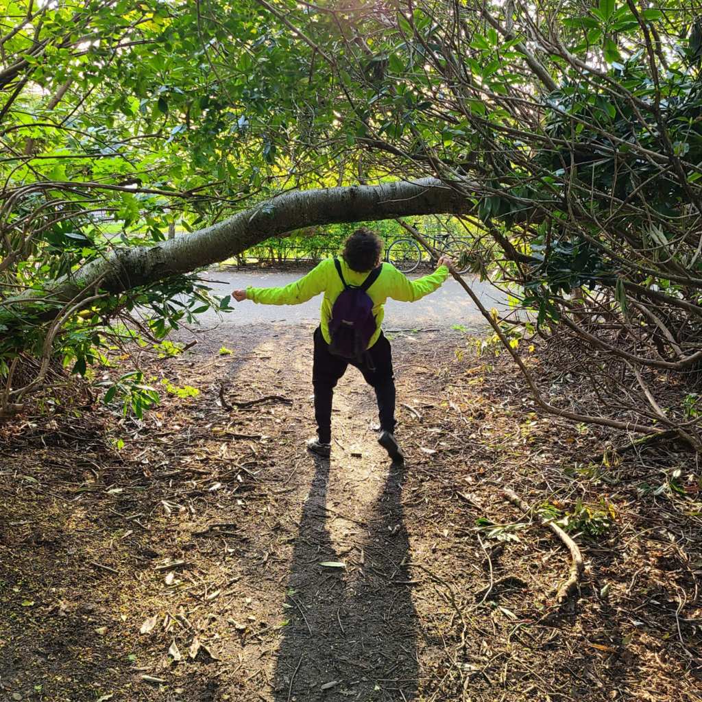 A person does the limbo under a tree branch. The sun casts a shadow behind them